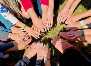 Une dizaine de mains d'adultes réunies en cercle sur l'herbe, au soleil